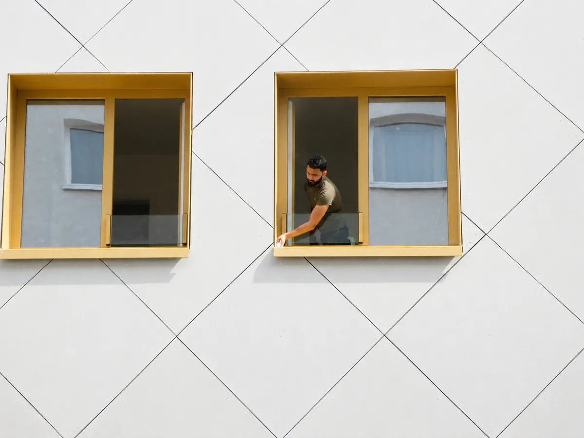 Weiße Neubaufassade mit gelb gerahmten Fenstern, ELMA-Mitarbeiter am geöffneten Fenster